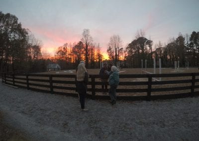 Horse riding arena at sunset with people talking near the fence.