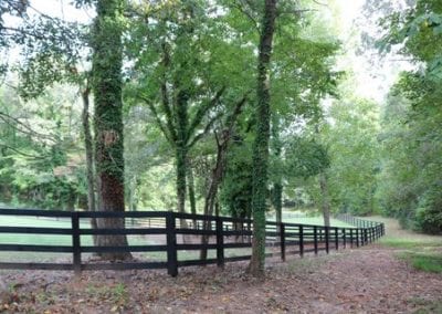 Scenic wooded trail with fencing at Millstone Stables, perfect for riding and outdoor activities.