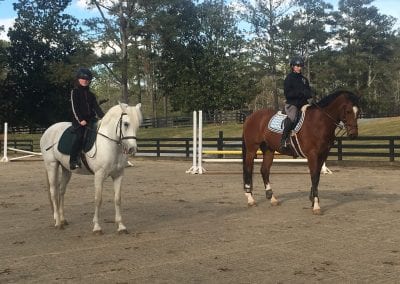 Horse riding lesson at Millstone Stables with two riders on horseback in a spacious outdoor arena.