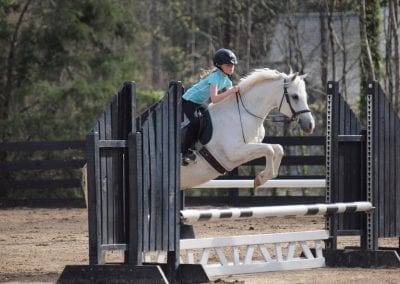 Young rider jumping over obstacle at Millstone Stables equestrian center.