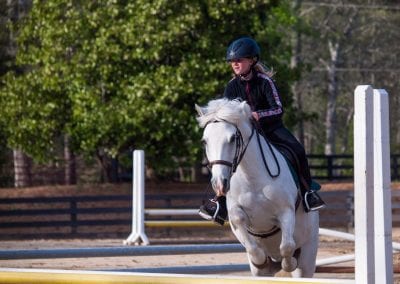 Horse riding lesson at Millstone Stables with a young girl in helmet riding a white horse in the out.